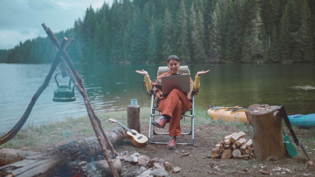 Happy woman shopping online while camping in front of a lake